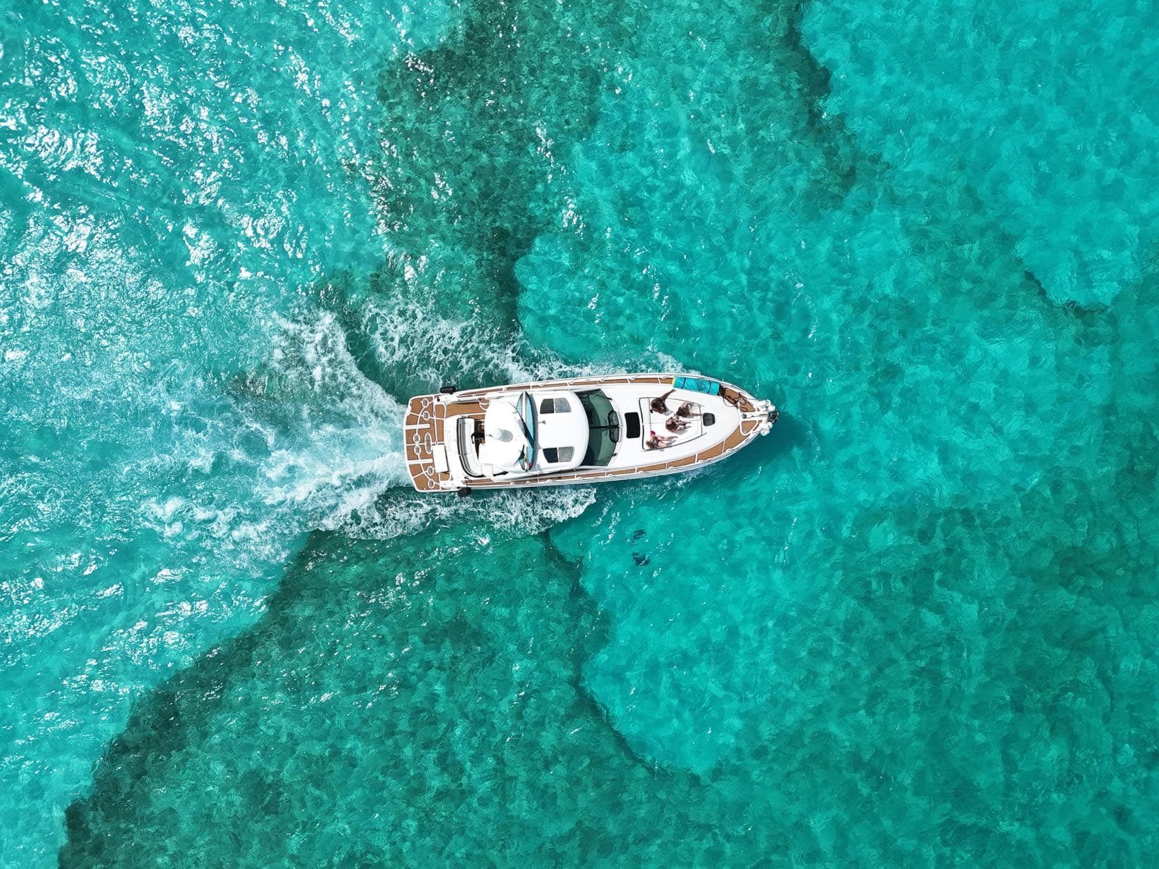 Yate de motor navegando sobre agua turquesa y arrecife, visto desde el aire