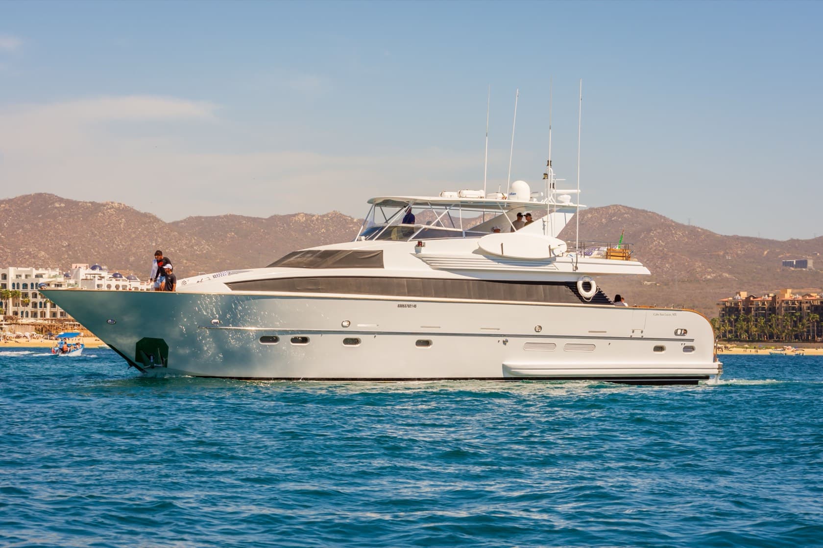 Yate de motor blanco con flybridge navegando frente a la costa de Cabo San Lucas