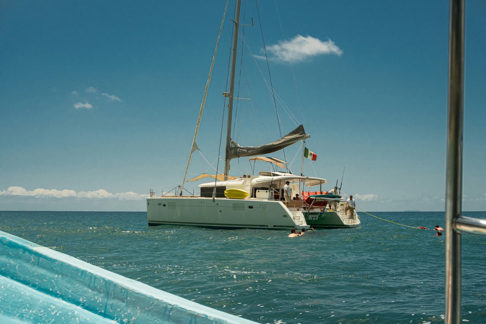Catamarán fondeado con bandera de México y gente nadando junto al casco