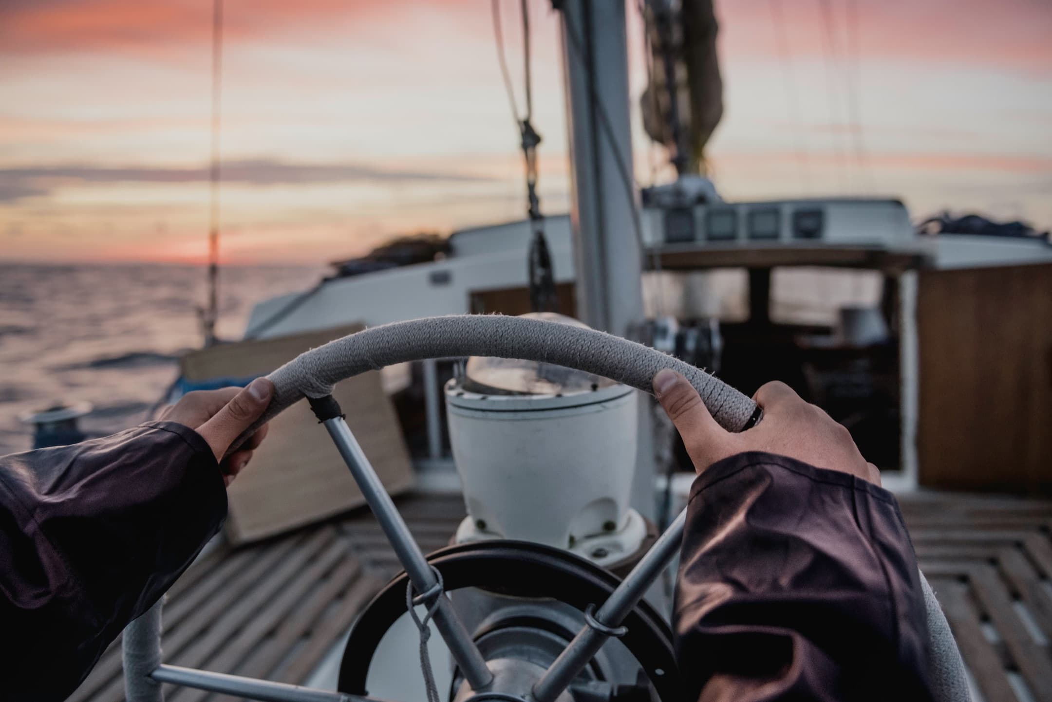 Hands on a sailboat's wheel at sunset