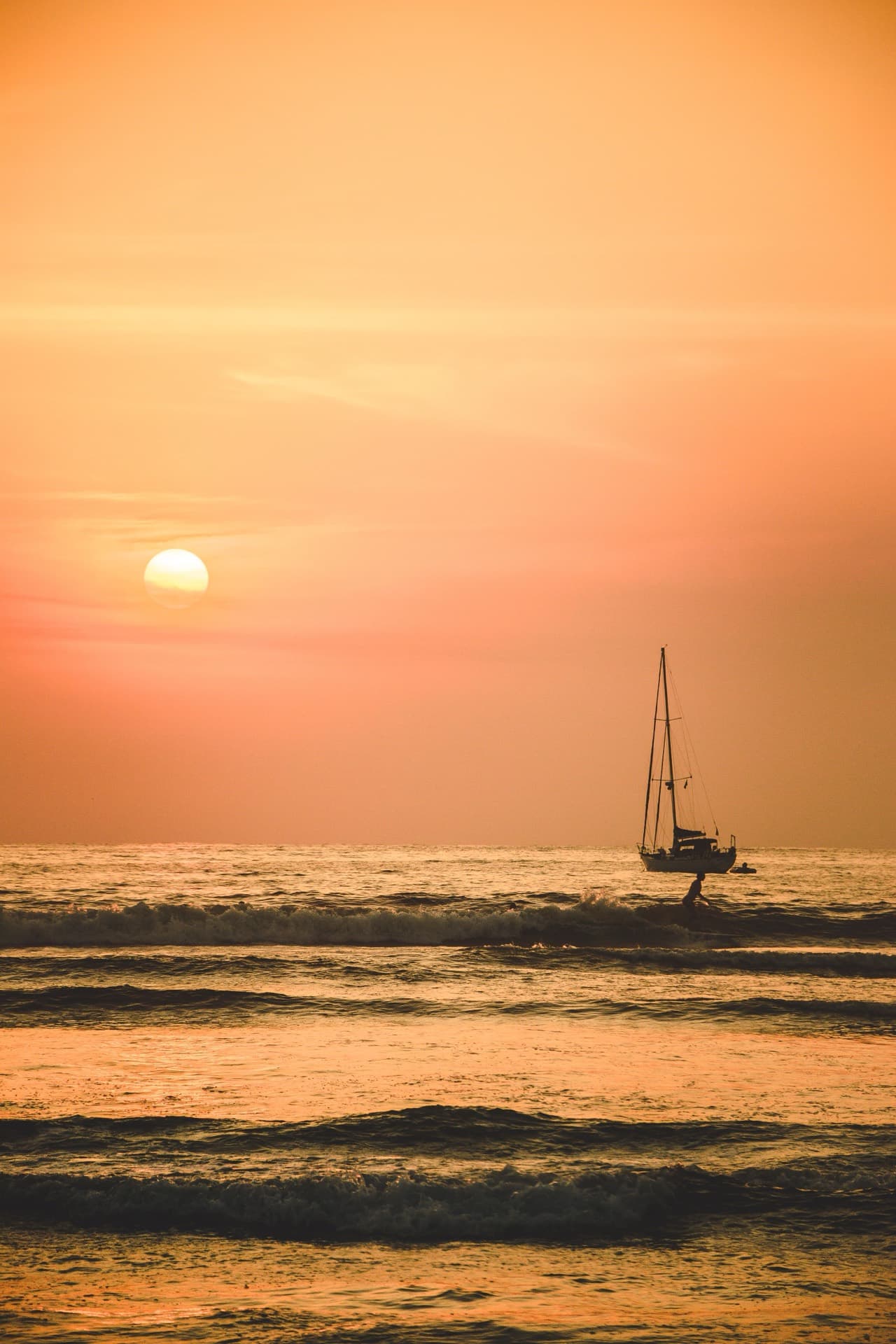 Velero en el horizonte con el sol bajo y el cielo naranja